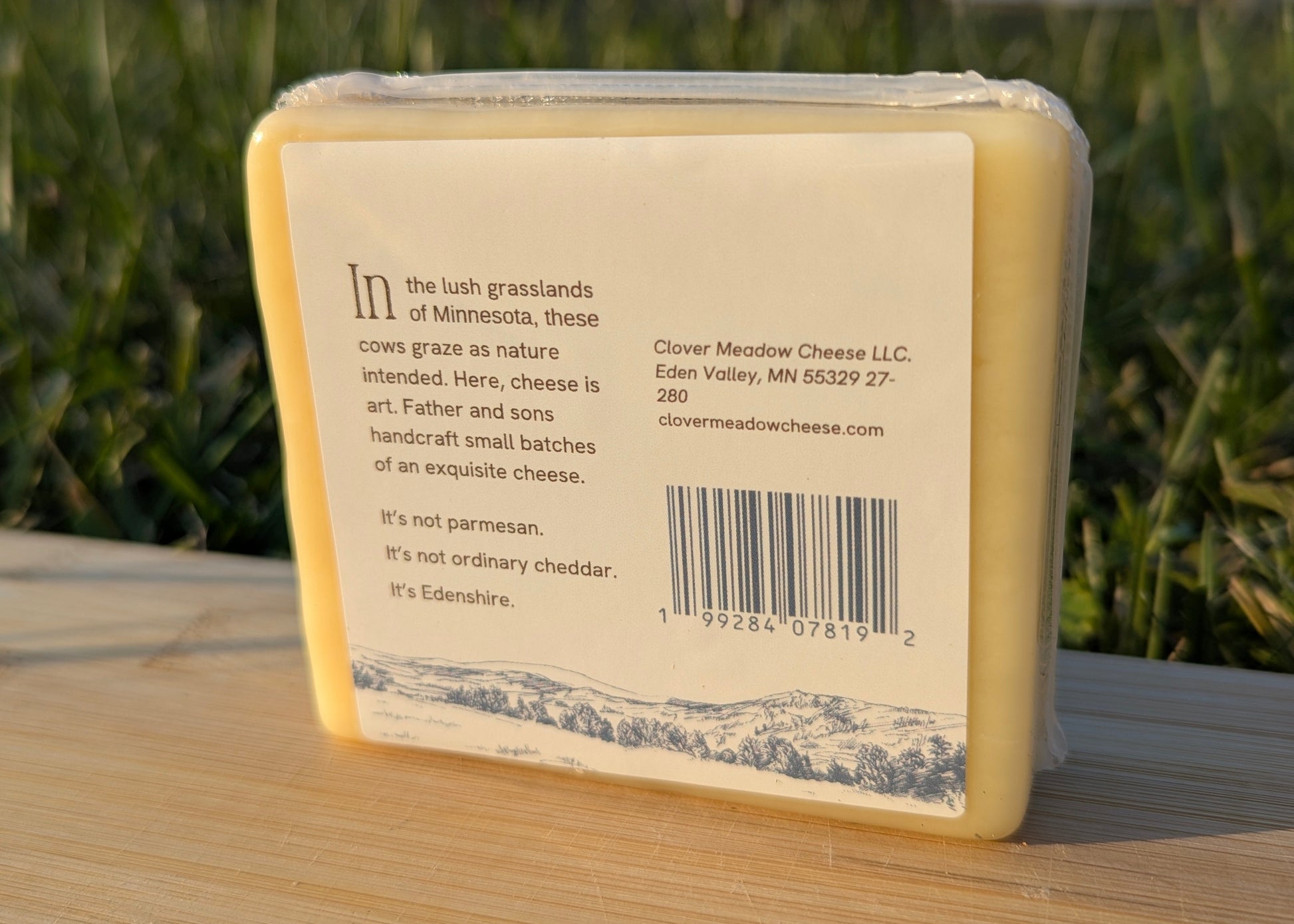 Cheese block with a label on a wooden surface and grassy background